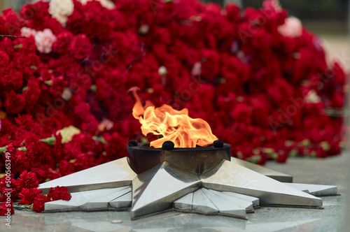 Festive background of Victory Day. Eternal flame against the background of carnations, a monument - a symbol of May 9, the memory of the war.