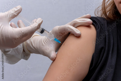 The doctor gives an injection into the girl's shoulder, an injection of a vaccine, a close-up. photo