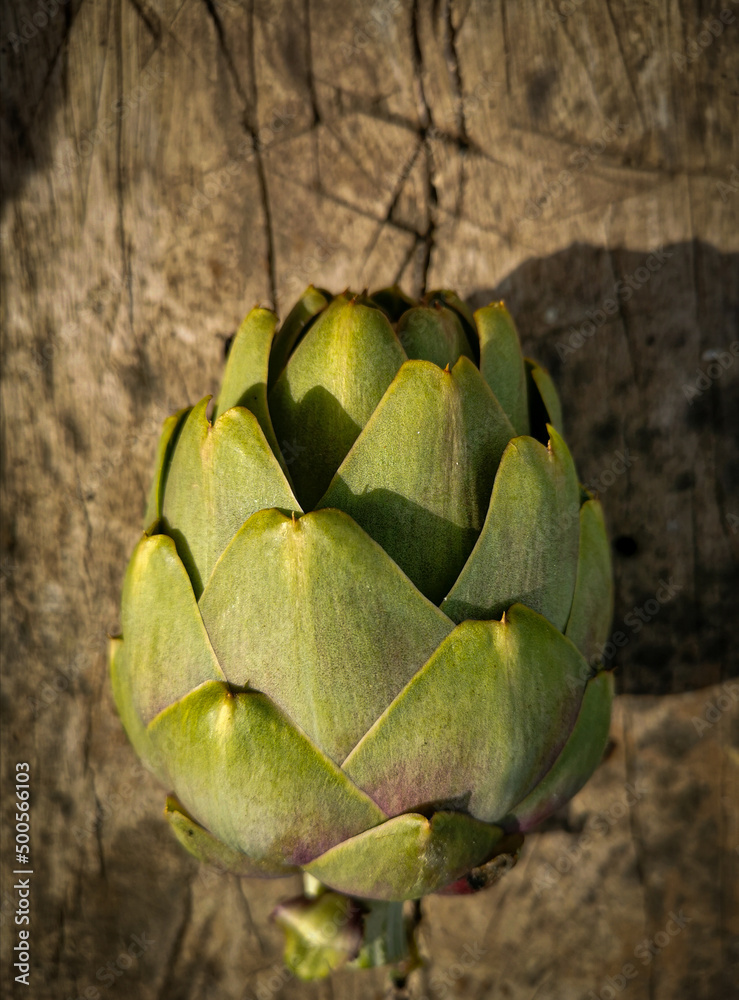 Obraz premium Fresh cut organic green yellow artichoke on a unfocused rough wooden board. Healthy food on rustic background