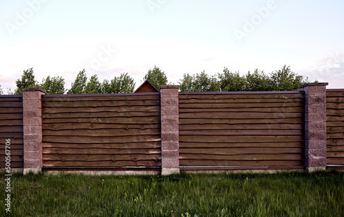 Brown wooden fence with block posts. Construction site. Corrugated surface. Private property fencing. Opaque hedge. Countryside backyard security exterior. Scandinavian, chalet or rustic style. DIY