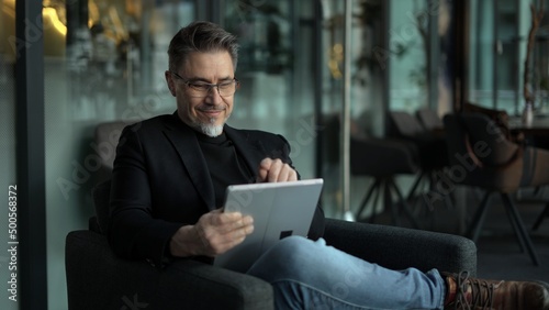 Businessman using tablet computer in office lobby or on cafe terrace. Happy middle aged man, entrepreneur, small business owner working online.