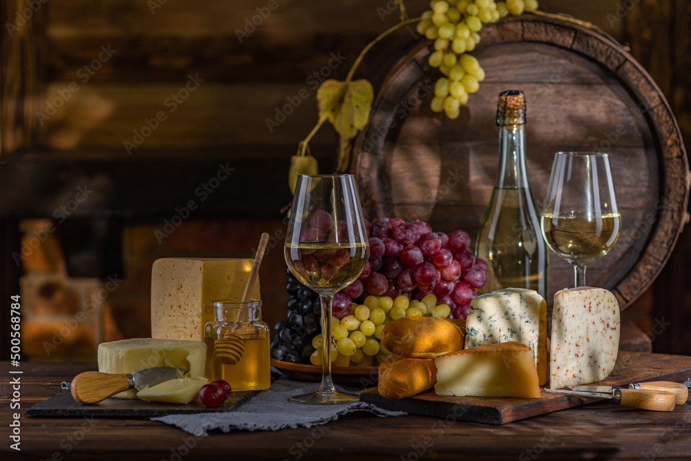Cheese and wine tasting still life. Glass of wine, bottle of wine, grape in front of the rustic wooden barrels for beverage in a dark wine cellar. Nuts, honey, dipper. Empty copy space, mock up