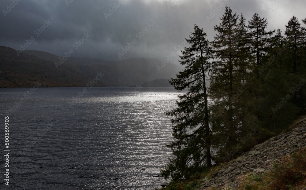 Shower over Haweswater. A moody shot taken from the footpath running along the western edge of Haweswater reservoir. A shower scuds past with the sun's rays cutting through. Shower over Haweswater. A moody shot taken from the footpath running along the western edge of Haweswater reservoir. A shower scuds past with the sun's rays cutting through.
