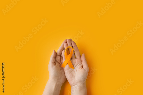Maio laranja. Hands holding an orange ribbon on an orange background. Concept of protection of children and adolescents from sexual violence and abuse. Orange may in Brazil, Portugal