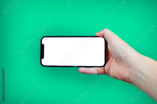 Hand holding the black smartphone with blank screen and modern frame less design on green colour background