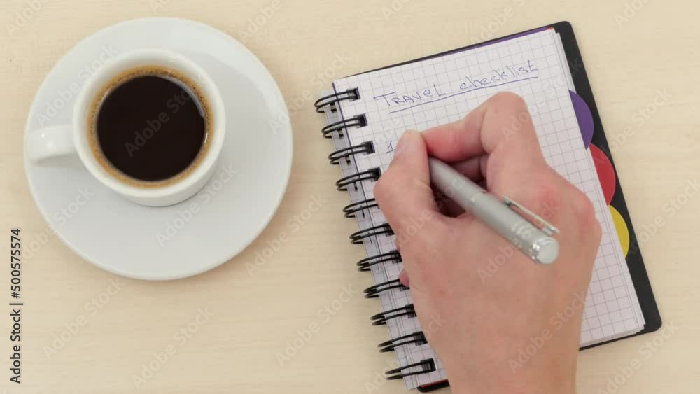 Male hand writes with a pen in a notebook on the table near a white cup of espresso coffee on a saucer travel checklist