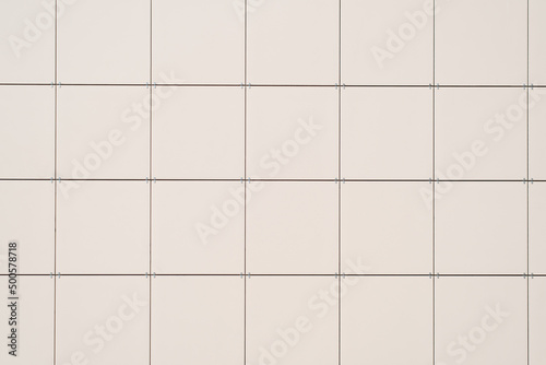 Tiled wall of large light ceramic tiles outdoors. Building facade close-up