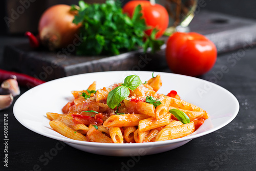 Classic italian pasta penne alla arrabiata with basil and freshly grated parmesan cheese on dark table. Penne pasta with chili sauce arrabbiata.