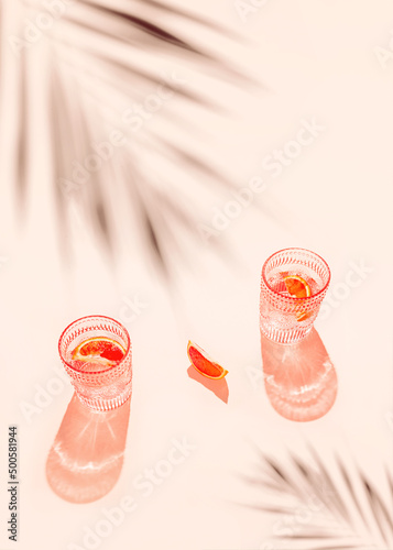 Creative composition made of two glasse with cocktail or lemonade on beige pastel background with lobule of bloody orange. Summer refreshment concept. Sunlit flat lay. Minimal style. Top view