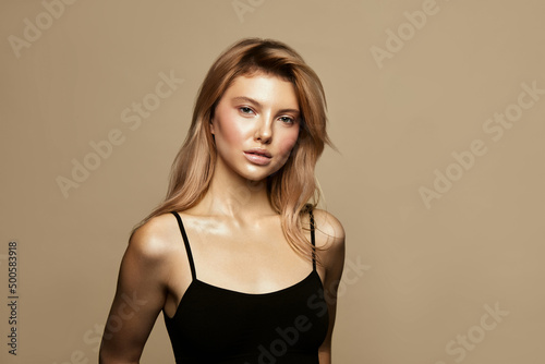 Blonde haired Woman Portrait with blue eyes and Healthy Long Shiny Wavy hairstyle touch skin face. Volume shampoo. Blond Curly permed Hair and bright makeup. Beauty salon and haircare concept.