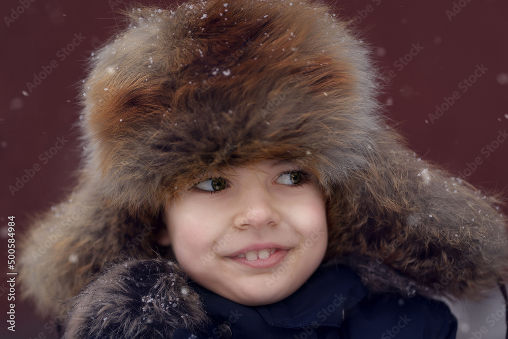 Portrait of a cute young boy with an old fashioned fur hat covered with snowflakes on the plum background. Portrait of a cute young boy with an old fashioned fur hat covered with snowflakes on the plum background.