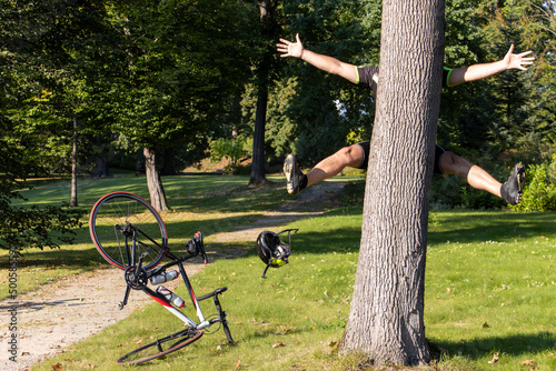 A cyclist bumps into a tree next to a path in a park.