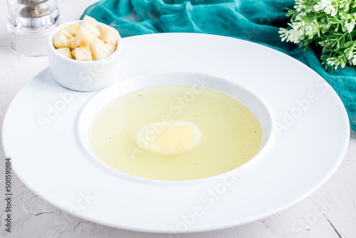 Chicken soup bouillon with egg and croutons on white bowl