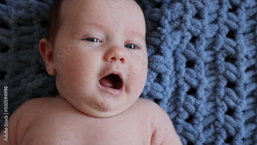 little girl with blue eyes on a knitted blue blanket smiles. advertising of children's goods