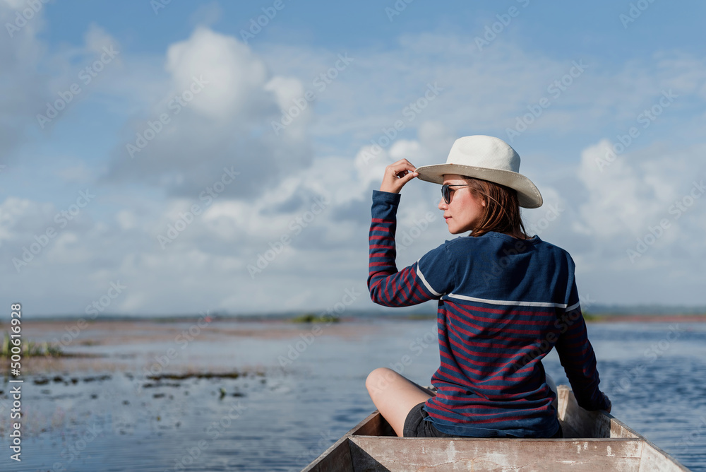 An Asian female tourist sits on a wooden boat, admiring the scenery of the river and the clear sky.