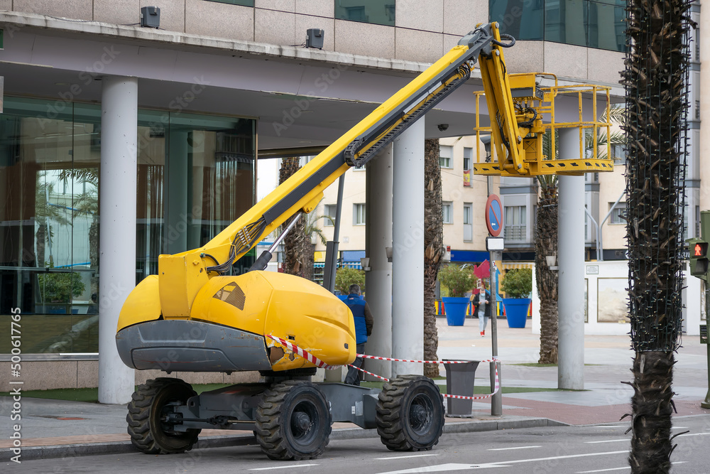 articulated boom lift of yellow color parked on the street with the empty basket
