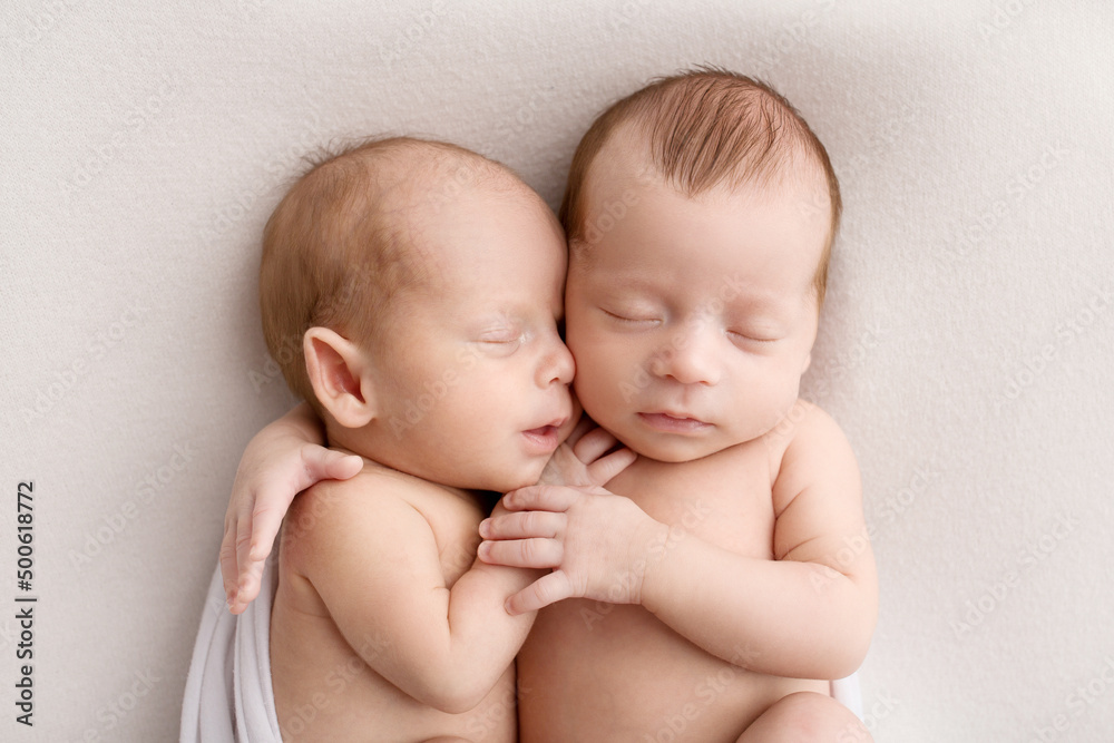 Tiny newborn twins boys in white cocoons on a white background. A newborn twin sleeps next to his brother. Newborn two twins boys hugging each other.Professional studio photography Tiny newborn twins boys in white cocoons on a white background. A newborn twin sleeps next to his brother. Newborn two twins boys hugging each other.Professional studio photography