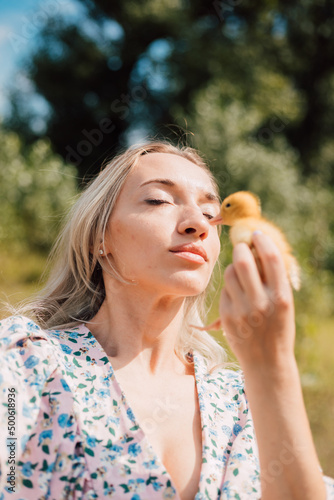 A young woman holds a duckling in her hands and closes her eyes enjoying 