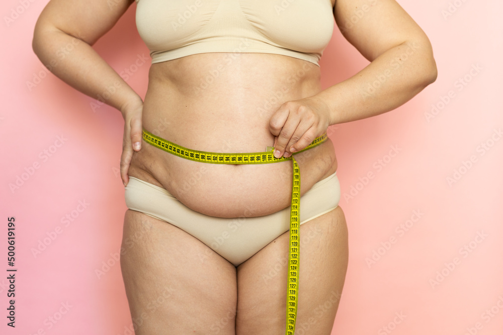 Cropped photo of fat woman tummy in underwear trying to lose weight.  Measuring by roulette tape belly, waistline, abdomen. Excess folds on her  stomach. Health care, obesity and overweight. Close-up. Photos