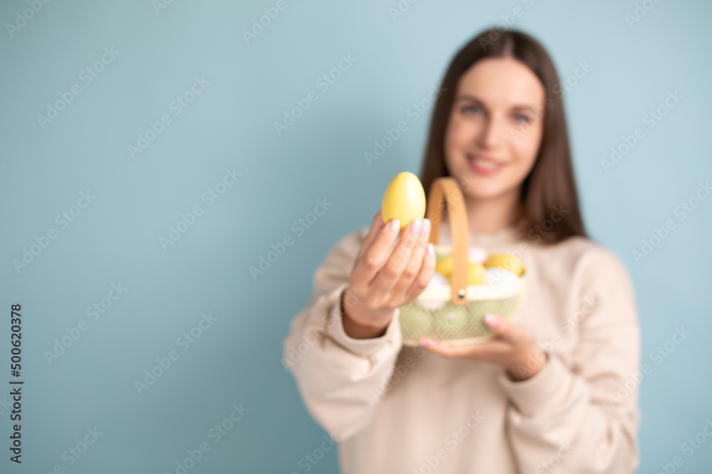 Cute brunette woman holds painted Easter eggs in basket in her hands, Easter, in the studio on a blue background. Cute brunette woman holds painted Easter eggs in basket in her hands, Easter, in the studio on a blue background.