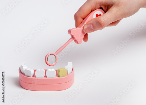 Hand with dental mirror magnifying sick tooth with plaque and caries. Dental care, oral hygiene, teeth cure concept. Children game at dentist. High quality photo