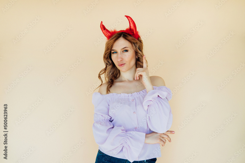 Portrait of a girl with wavy hair, in a devil costume for Halloween near a beige wall. Portrait of a girl with wavy hair, in a devil costume for Halloween near a beige wall.