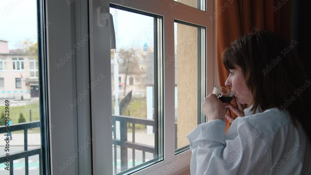 cinematic brunette woman drinking coffee near the window and looking at the street, woman drinking tea looks out the window and thinks cinematic brunette woman drinking coffee near the window and looking at the street, woman drinking tea looks out the window and thinks