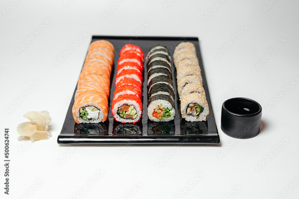 Sushi, rolls. Chinese and Asian cuisine, sets of rolls of ginger and soy sauce lie on a black board with chopsticks. Sushi is made in sets