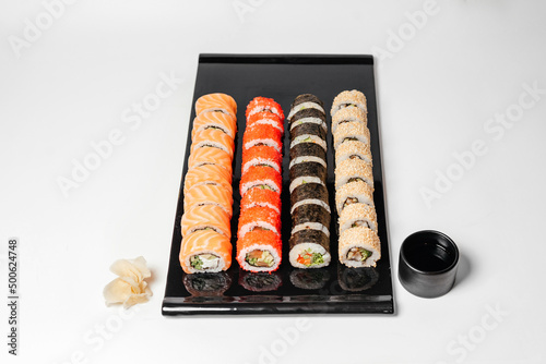 Sushi, rolls. Chinese and Asian cuisine, sets of rolls of ginger and soy sauce lie on a black board with chopsticks. Sushi is made in sets