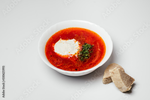 Ukrainian traditional dish hot delicious borsch with sour cream and fresh herbs, with meat in a plate on a white background