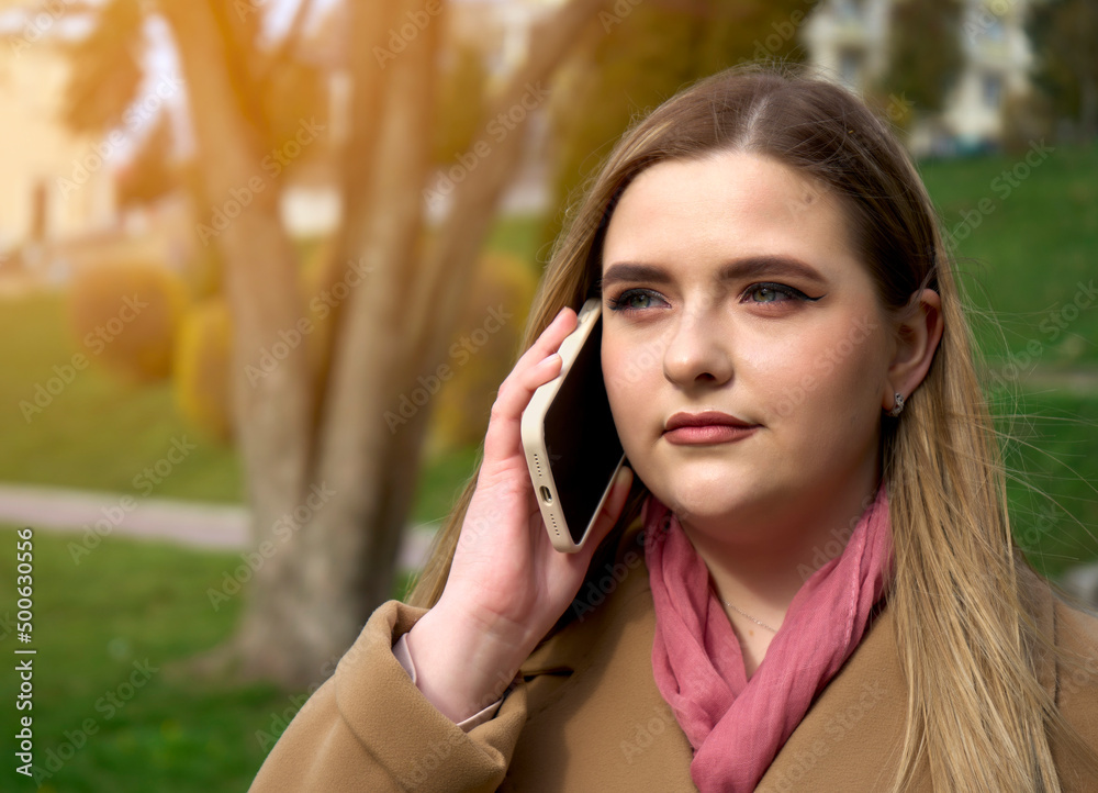 Portrait of serious young woman talking on mobile phone while walking at city street. Girl having business conversation on cell phone Portrait of serious young woman talking on mobile phone while walking at city street. Girl having business conversation on cell phone