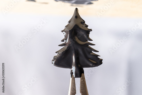 pinza sosteniendo figura de pino cubierta de pintura negra fresca espesa irregular con fondo claro