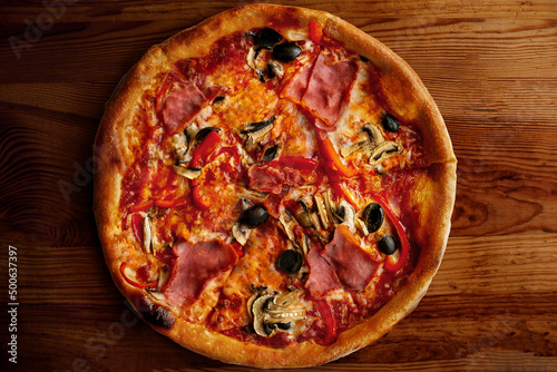 Pizza with ham mushrooms and olive on wooden table