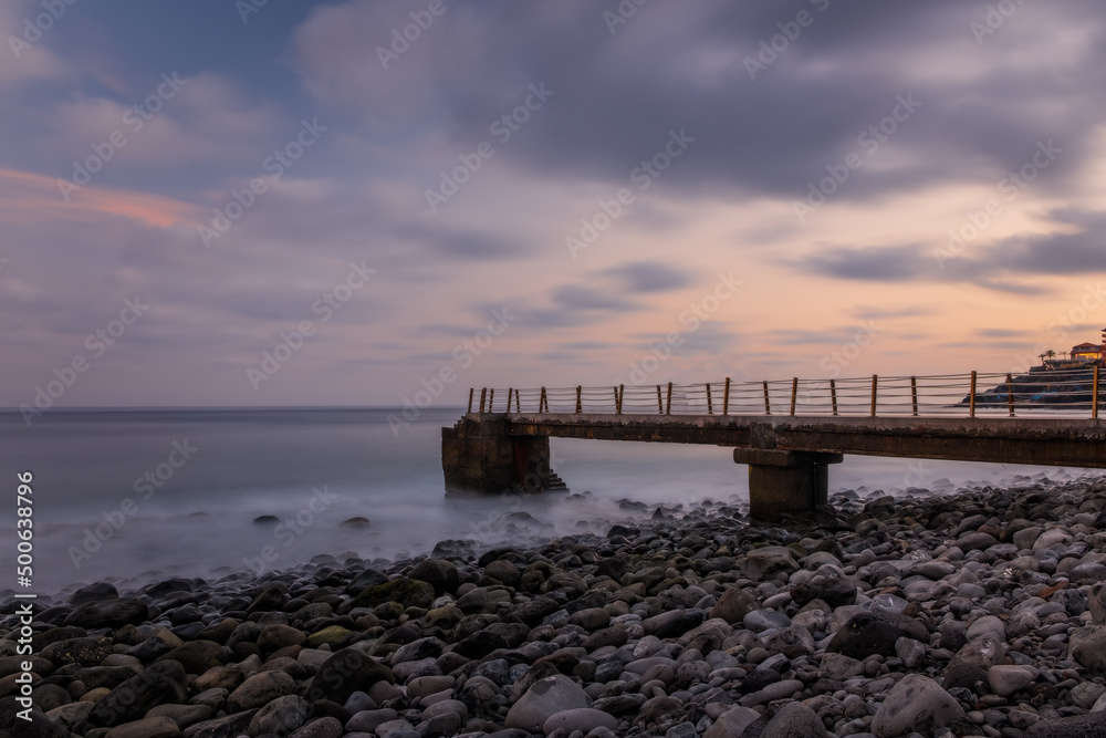 Jetty at pebbles beach near Canico at Portugese Madeira Island at sunset time. October 2021. Long exposure picture