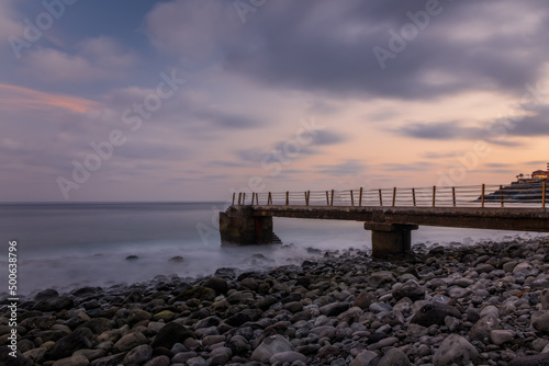 Jetty at pebbles beach near Canico at Portugese Madeira Island at sunset time. October 2021. Long exposure picture