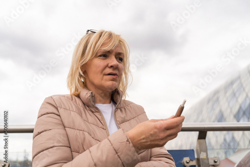 Middle aged blonde European woman smoking heated tabacco e-cigarette outdoors on the street. Alternative smoking way photo