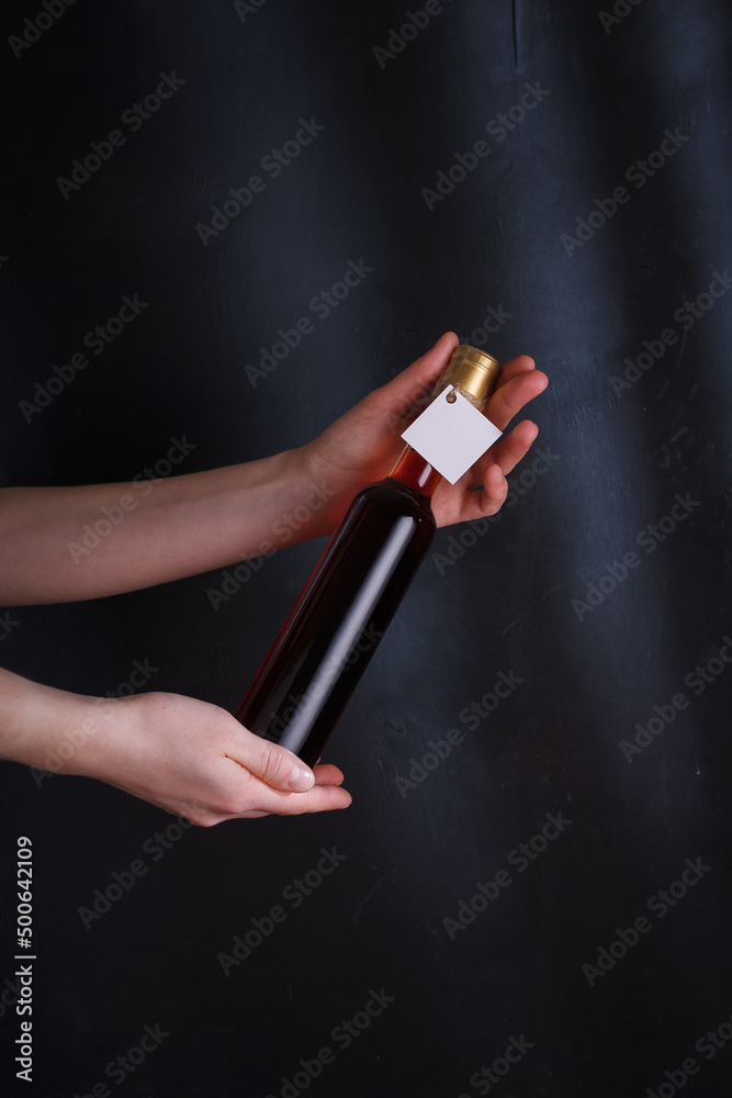 female hands holding 250 ml bottle of red wine with mock up label, no brand on black background. Alcohol drink, copy space