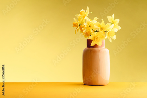 Yellow flowers in a glossy decorative vase on a yellow background against a yellow background. The concept of minimalism. Poster for advertising. Place for text
