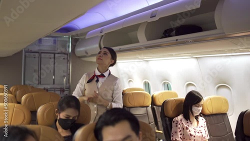 The female crew is helping passengers lift their luggage in the in-flight luggage compartment and lock it down in preparation for takeoff in tourist travel concept. photo