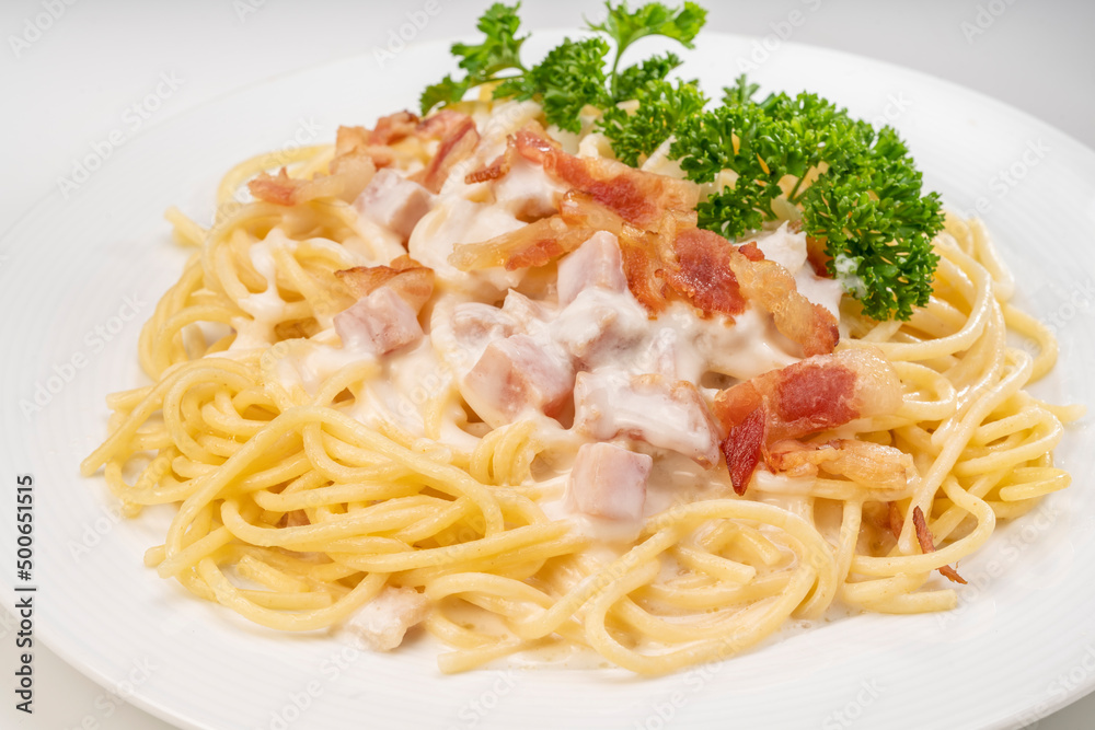 Spaghetti carbonara with Crispy Bacon and Ham on white plate on white background, Carbonara pasta with parmesan cheese and cream sauce, Traditional italian cuisine.