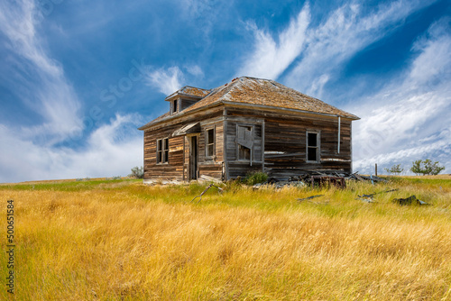 Blue sky over an old, abandoned home surrounded by junk on the prairies of Saskatchewan 