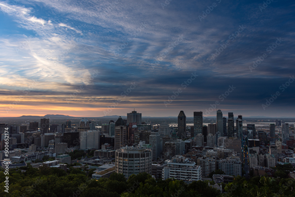 Panorama of the Montreal skyline at dawn during a warm summer morning, skyscrapers, orange and blue sky before sunrise with grey cirrus clouds, seen from the Kondiaronk belvedere