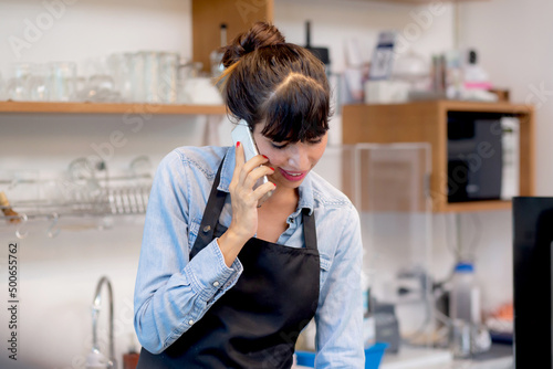 Young woman is barista talking on phone for order and using tablet computer and delivery online in the cafe, entrepreneur and small business, employee or owner retail, startup business concept.