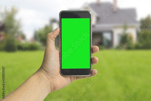 Hand holding green screen phone on summer blurred background
