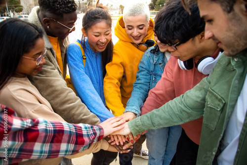 Group of multiracial college students stack hands together in a circle outdoors.