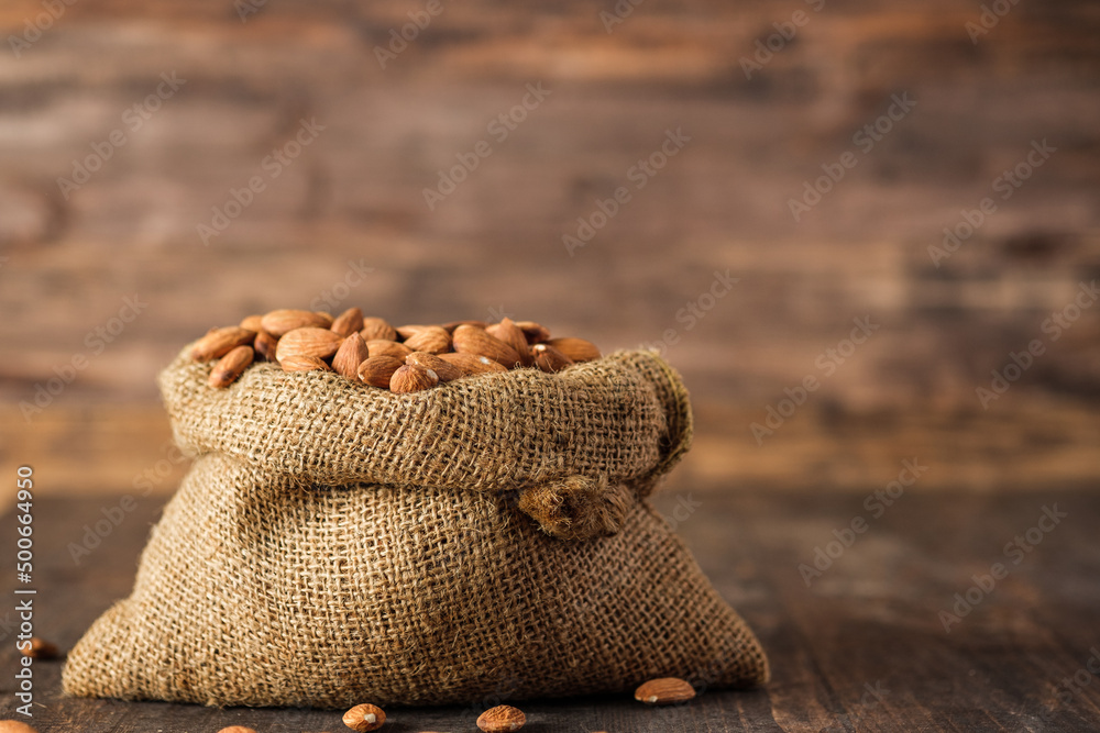 Obraz premium Almonds in sack bag on wood table.organic raw material