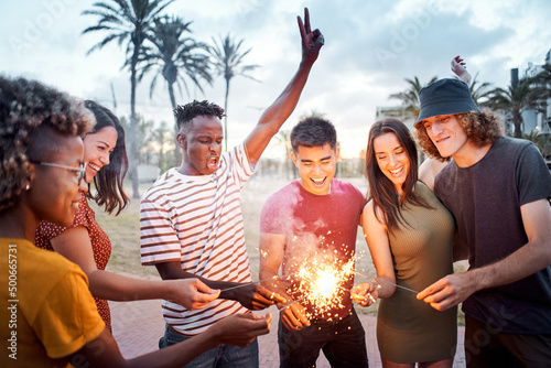 Group of friends light some sparklers at sunset. Young multiethnics celebrating together. Concept of summer, integration, happiness, free time, friendship. #500665731