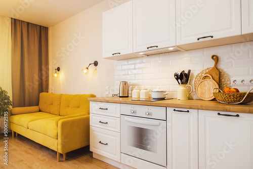 small studio apartment with yellow sofa, white kitchen. Cozy light on