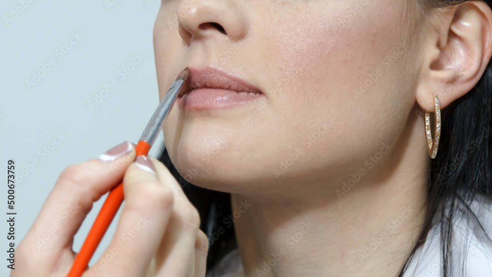 Makeup artist applying lipstick on a model lips