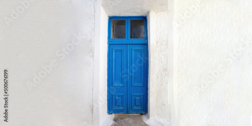 Blue wooden door on empty white wall background. Greek island house front view.